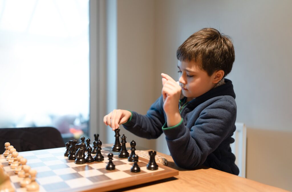 Young boy developing chess strategy, playing chessboard game with friend or family at home