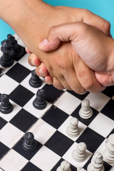 Side view close up of two chess players shaking hands over chess board